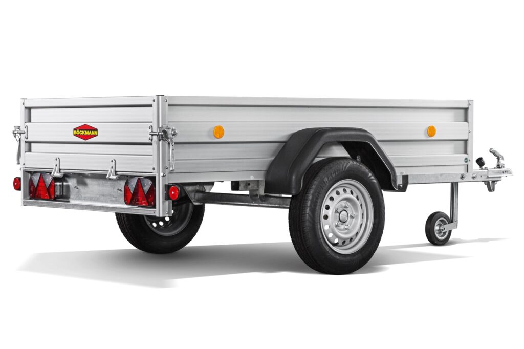 Ein silberner, einachsiger Nutzfahrzeuganhänger mit Metallwänden, einem schwarzen Radkotflügel, Rückleuchten, Reflektoren und einem kleinen vorderen Stützrad, von hinten links gesehen.